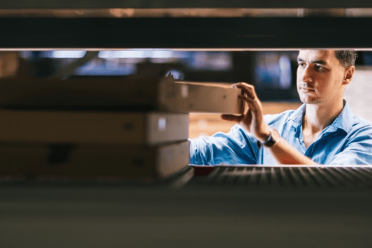 Warehouse worker organizing stacked boxes on a shelf, representing hands-on inventory control and the importance of accurate reordering and inventory level monitoring.