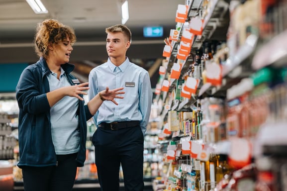 Retail workers discussing shelf strategy in a supermarket aisle, highlighting the importance of merchandise planning software in category management, pricing, and allocation decisions.