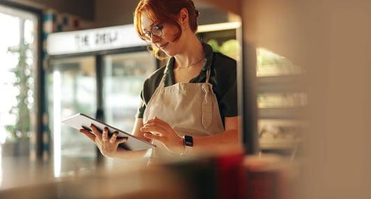 A cheerful store owner using a digital tablet in her grocery store, checking inventory levels and managing stock with inventory replenishment software.