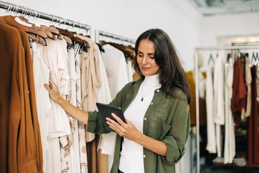 Boutique owner conducting quality control using a tablet in her clothing store.
