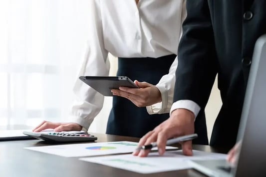 Business professionals reviewing financial performance reports with a tablet and calculator to evaluate investment returns.