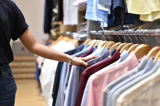 Shopper browsing a rack of colourful shirts in a clothing retail store, highlighting apparel selection and merchandising.