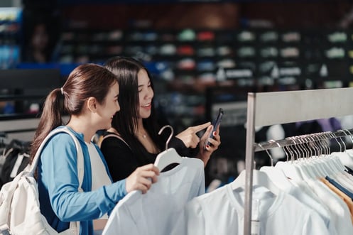 Modern consumers comparing prices and product details on smartphone in-store, illustrating retail pricing optimization and adaptive pricing behavior.