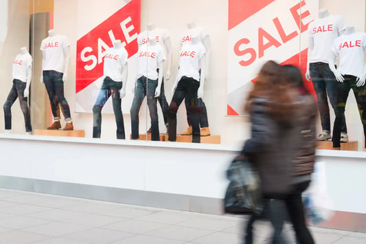 Shoppers walking past a sale in a storefront window.