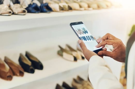 Customer browsing shoe options on a smartphone in-store, showcasing retail technology and mobile commerce