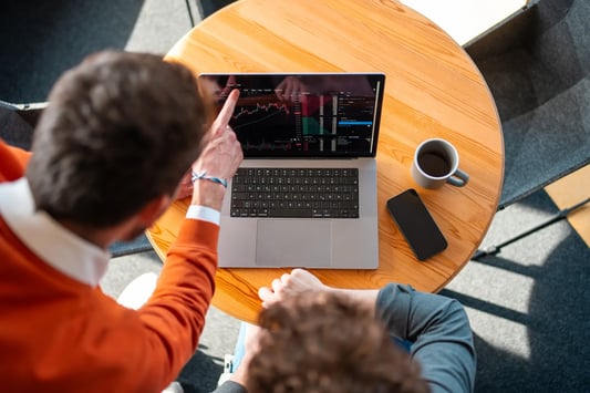Retailer analyzing market data on a laptop, discussing investment strategies.