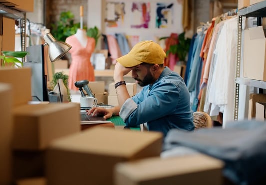 Retail store manager holding head in hands, frustrated with pricing or inventory issues.