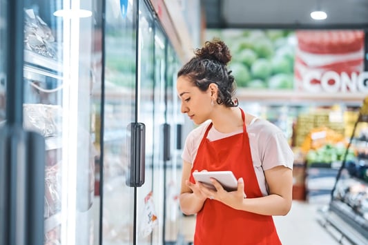 Worker in a supermarket aisle selecting perishable food items while considering freshness and expiry dates, highlighting inventory rotation and food waste reduction.