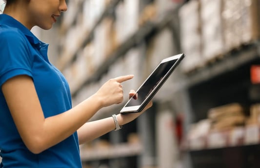 warehouse employee in blue uniform reviewing a checklist while organizing parcel boxes, supporting inventory and fulfillment operations.
