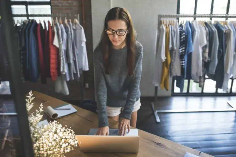 A retail merchant uses technology to support retail growth and retail advancement, surrounded by clothing racks in a modern store setting.