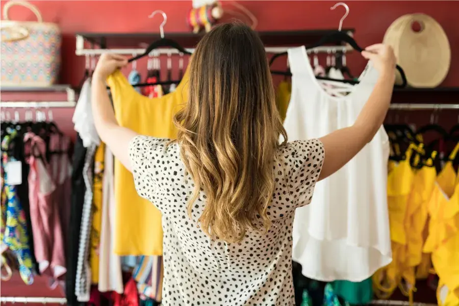 Woman comparing two dresses in a store, reflecting assortment strategy, product mix, and category management decisions in retail.