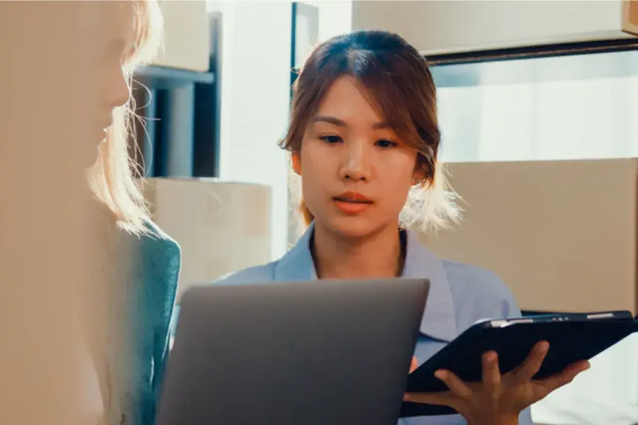 Retail employee using a laptop and tablet to review data for inventory optimization, including demand forecasting, reorder points, and inventory control strategies.