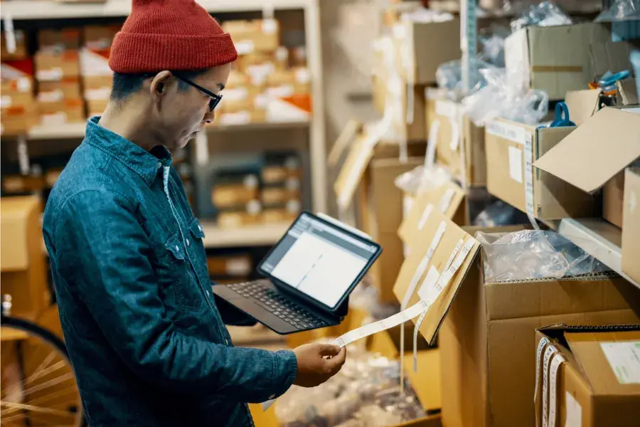 Retail worker using a tablet to check inventory boxes, illustrating assortment planning, SKU rationalization, demand forecasting, and data-driven decisions in omnichannel retailing.