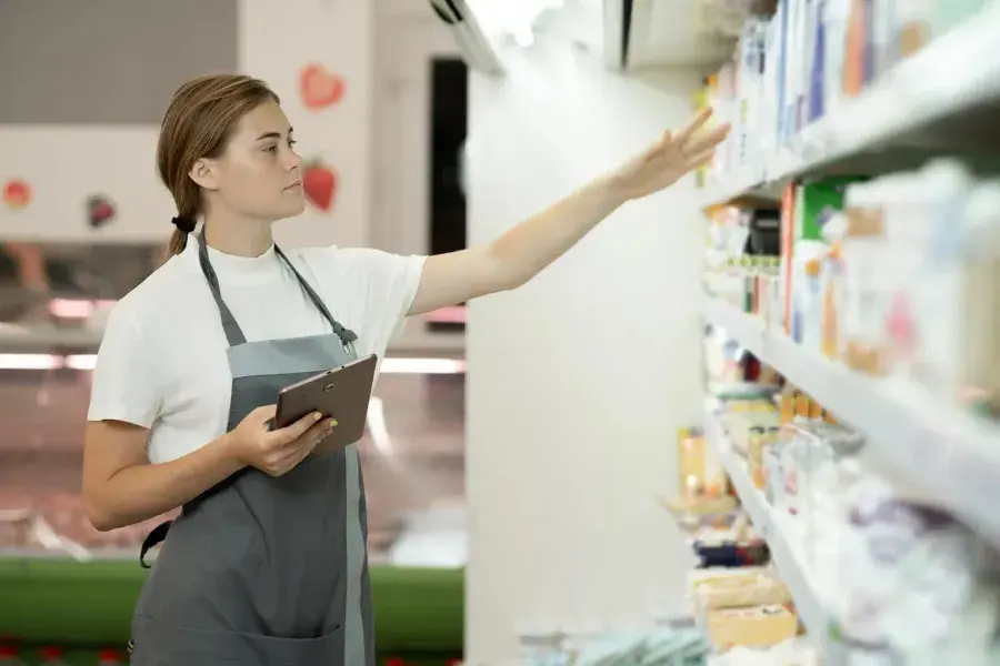 A grocery store worker uses a digital tablet to monitor inventory and manage stock levels.