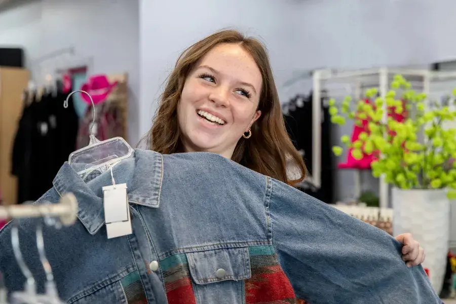 Smiling customer holding a denim jacket in a retail store, representing price optimization through dynamic pricing, customer segmentation, and competitive pricing strategies.