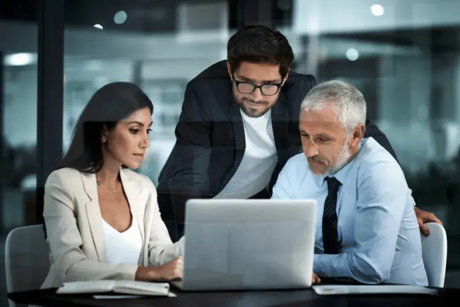 Three retail business professionals collaborating in an office, reviewing data on a laptop checking demand forecast accuracy.