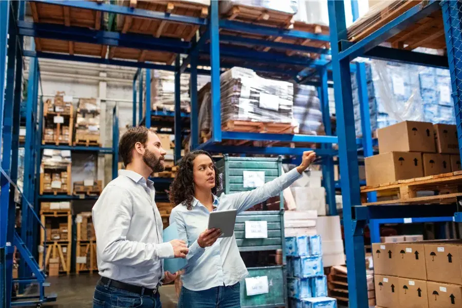 Two warehouse employees using a tablet to review stock levels, illustrating how inventory planning software supports inventory optimization, real-time inventory tracking, purchase order management, and automated inventory replenishment to prevent stock imbalances.