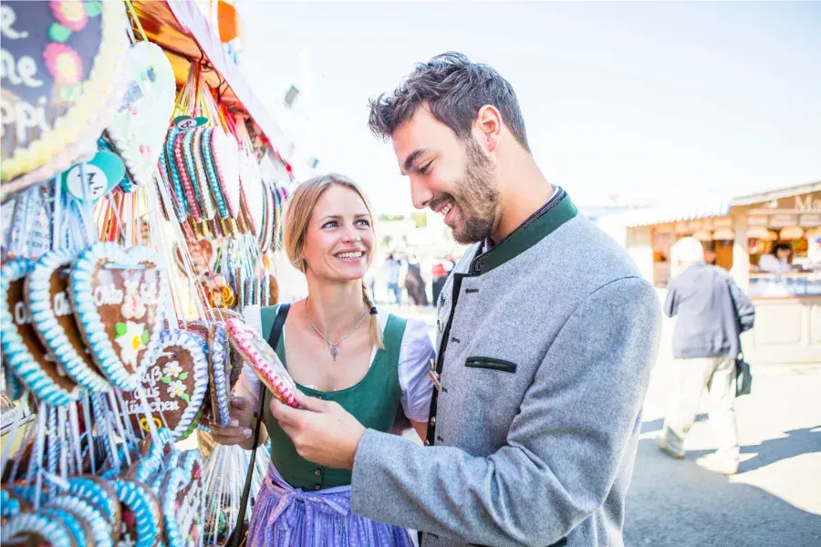 Couple in traditional Bavarian clothing shopping at an Oktoberfest market stall, symbolizing retail planning, demand forecasting, inventory management, product assortment, and customer experience in a competitive market.