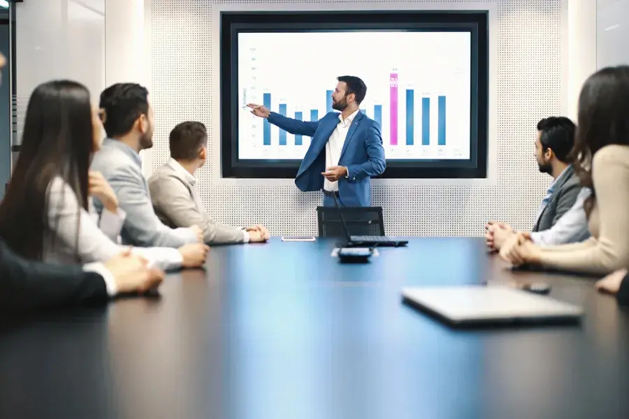 An inventory planner presents sales data and demand forecasts to a team, highlighting inventory levels, cash flow, and supply chain decisions. The meeting focuses on optimizing stock, cutting costs, and effective inventory planning for retail operations.