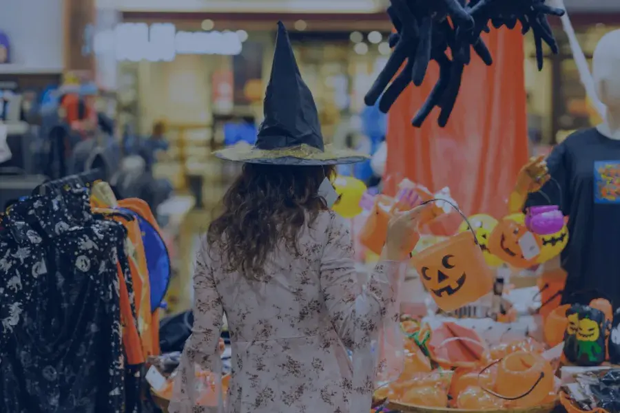 Shopper in a witch hat browsing Halloween-themed retail display, highlighting AI-powered demand forecasting and allocation strategies for seasonal inventory.