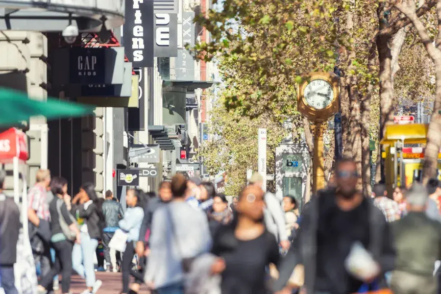 Busy urban shopping street with various store signs and pedestrians, representing strategic retail decisioning through real-time insights on consumer preferences, inventory levels, and retail operations to improve the shopping experience, pricing strategy, and overall customer satisfaction.