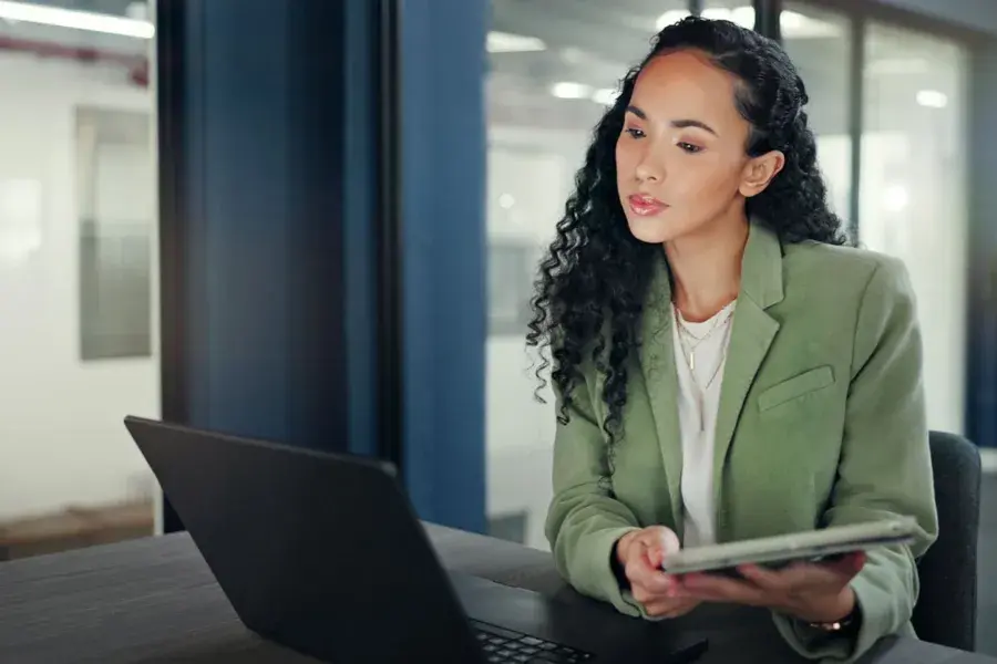 A businesswoman uses a tablet and laptop in a modern office, representing retail agentic AI driving real-time optimization, AI-driven insights, and decision-making across supply chain and financial services through autonomous systems, predictive analytics, and human-in-the-loop collaboration.