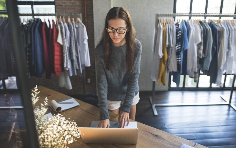 A retail merchant uses technology to support retail growth and retail advancement, surrounded by clothing racks in a modern store setting.