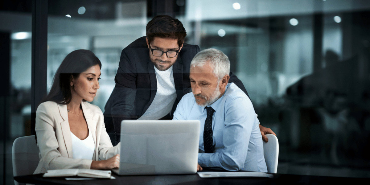 Three retail business professionals collaborating in an office, reviewing data on a laptop checking demand forecast accuracy.