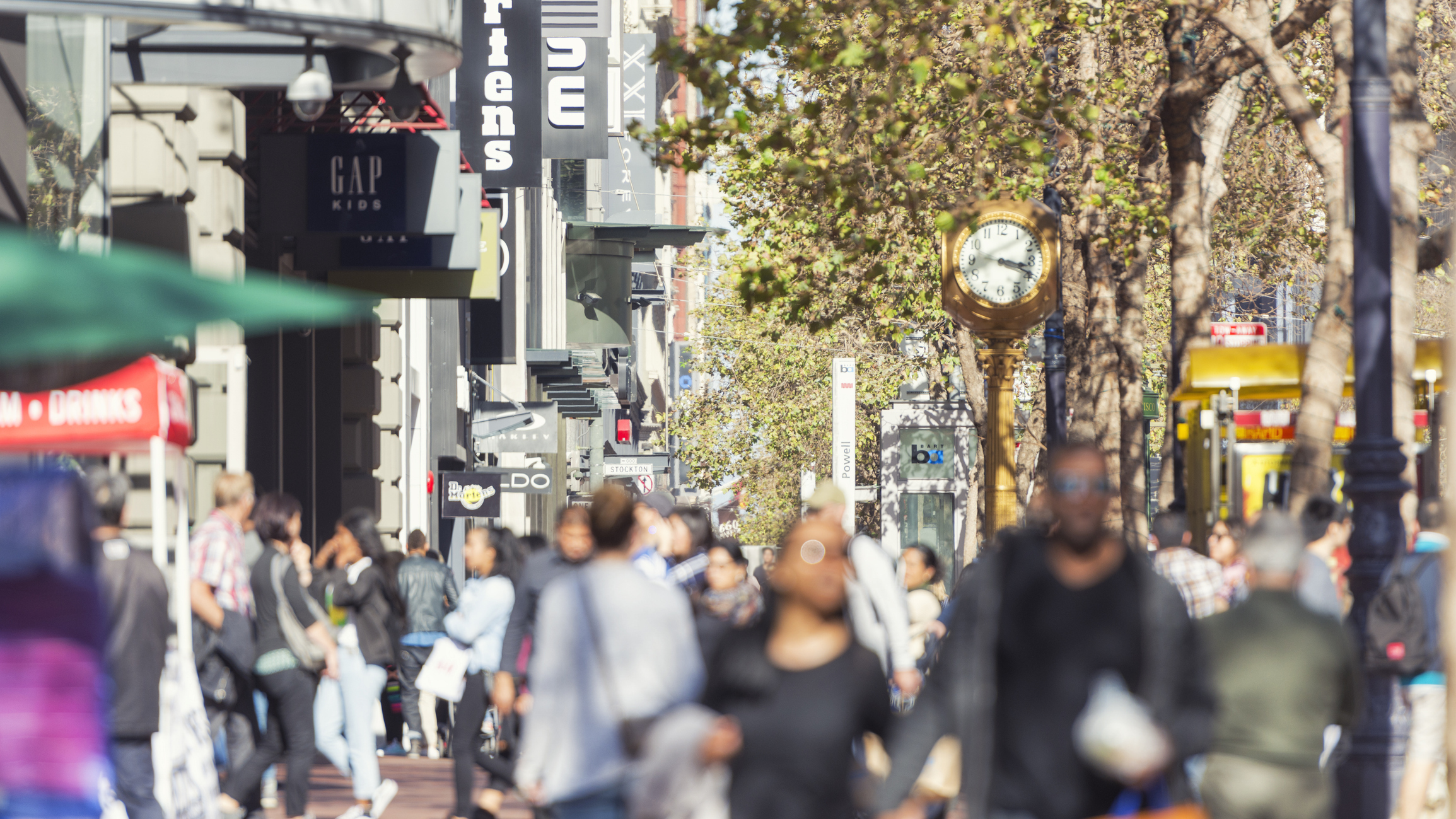 Busy urban shopping street with various store signs and pedestrians, representing strategic retail decisioning through real-time insights on consumer preferences, inventory levels, and retail operations to improve the shopping experience, pricing strategy, and overall customer satisfaction.