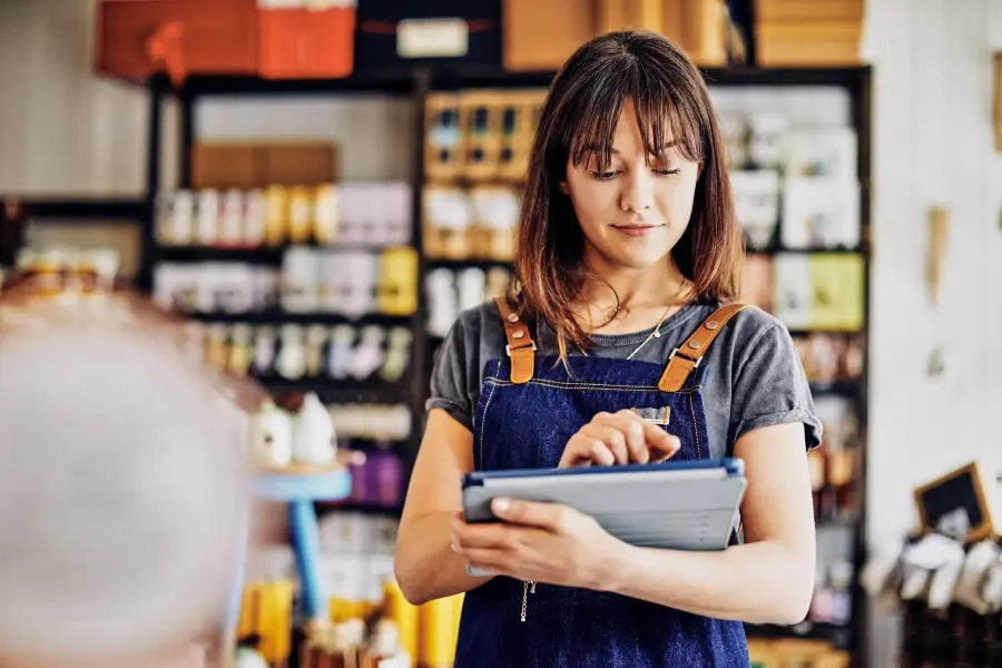 Retail planner using a digital tablet while reviewing demand forecasting data in a store environment.