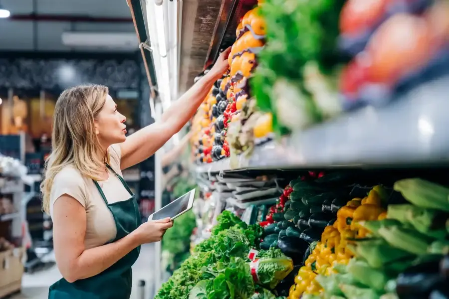 Grocery store employee checking perishable inventory stock levels on a shelf to manage replenishment and reduce food waste.