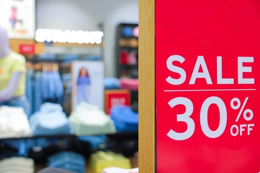 Red sale sign advertising 30% off in a clothing retail store, with apparel displays in the background.