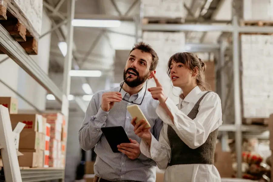 Retailers working together at a warehouse checkout station, reviewing inventory and logistics processes in a busy distribution environment.